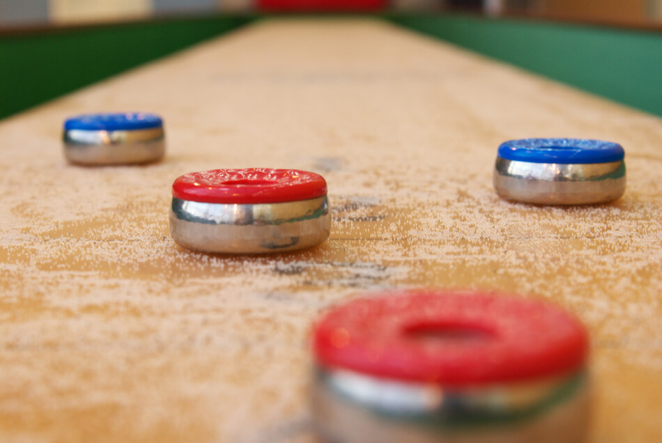 2 røde og 2 blå shuffleboard brikker glider hen ad et shuffleboard bord