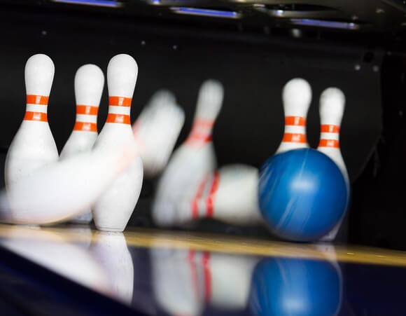 Blå bowlingkugle vælter kegler i en strike